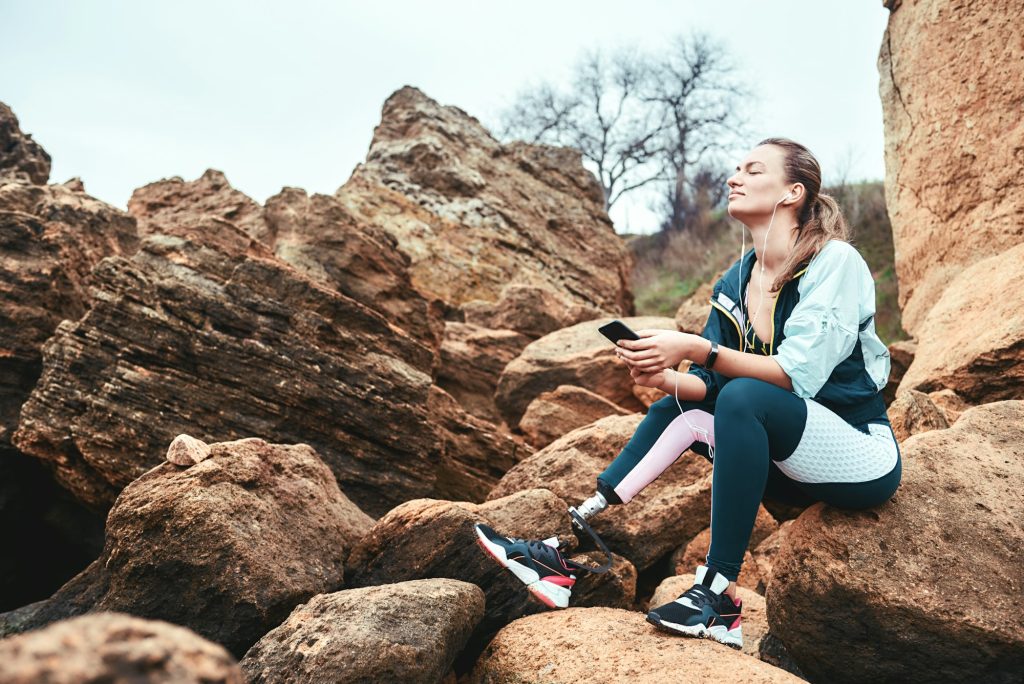 Feeling free. Happy disabled women in sport wear with leg prosthesis sitting on the boulders with